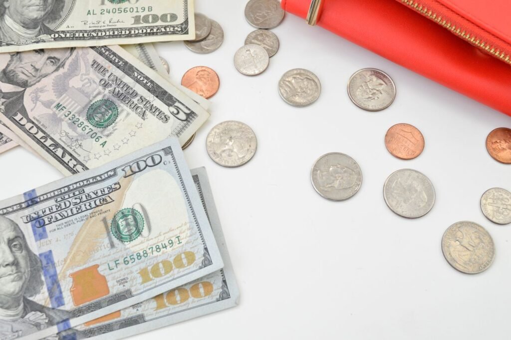 Detailed image of US dollars and coins spread with a red wallet on a white surface, ideal for financial concepts.