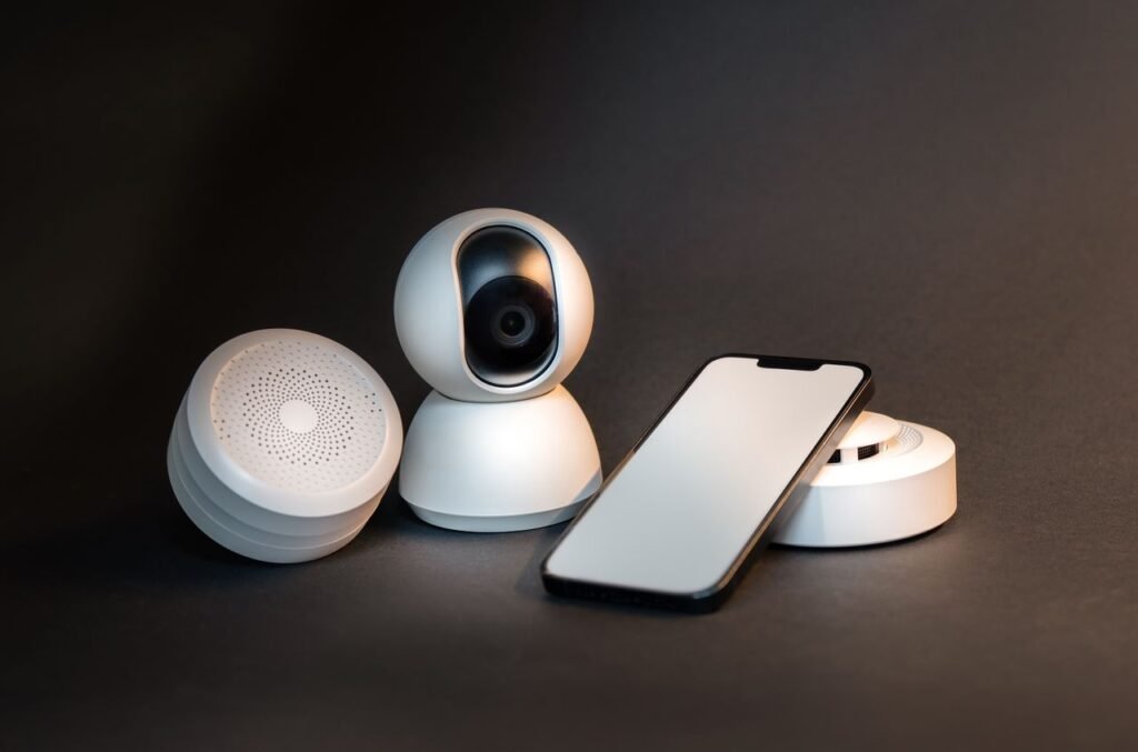 How Smart Home Technology Will Change Lives? A sleek smartphone with modern smart home devices on a minimalist gray background.