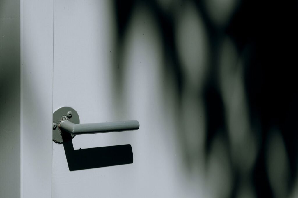 Close-up of a modern steel doorknob with dramatic light and shadow contrast outdoors.