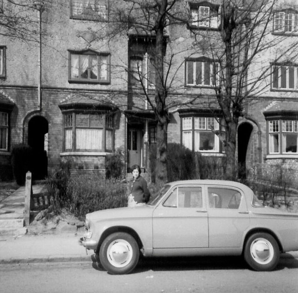 Black and white photo of a classic car in front of historic urban buildings.