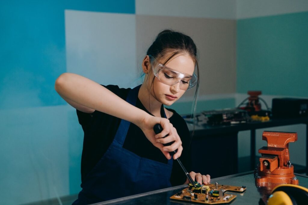 Woman with protective goggles soldering electronic components indoors.