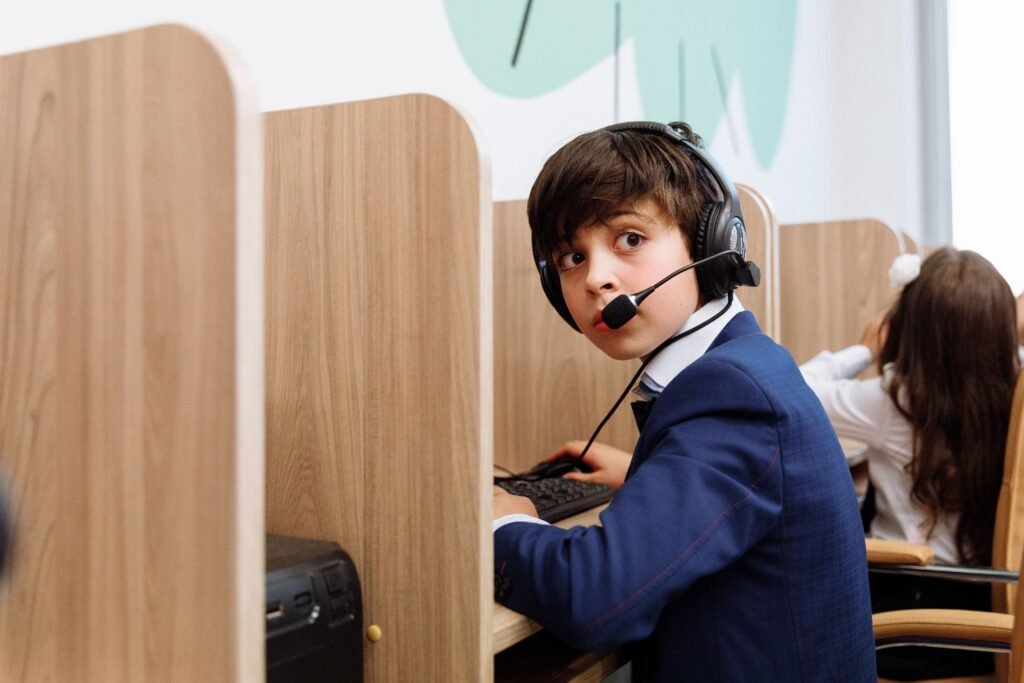 Emergency Procurement K12 Education Technology IT Hardware Distribution A boy in a blue suit wearing headphones focused in an educational setting with wooden cubicles.